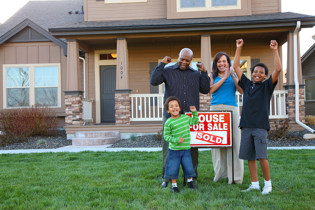 family standing outside of a brown house and a sold sign