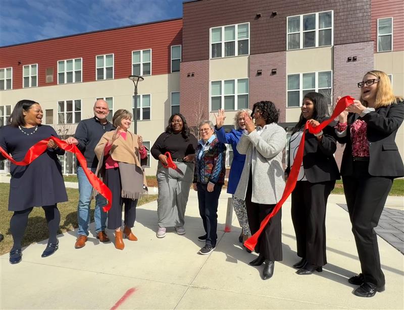 A group of people celebrate a ribbon cutting outside a new rental development