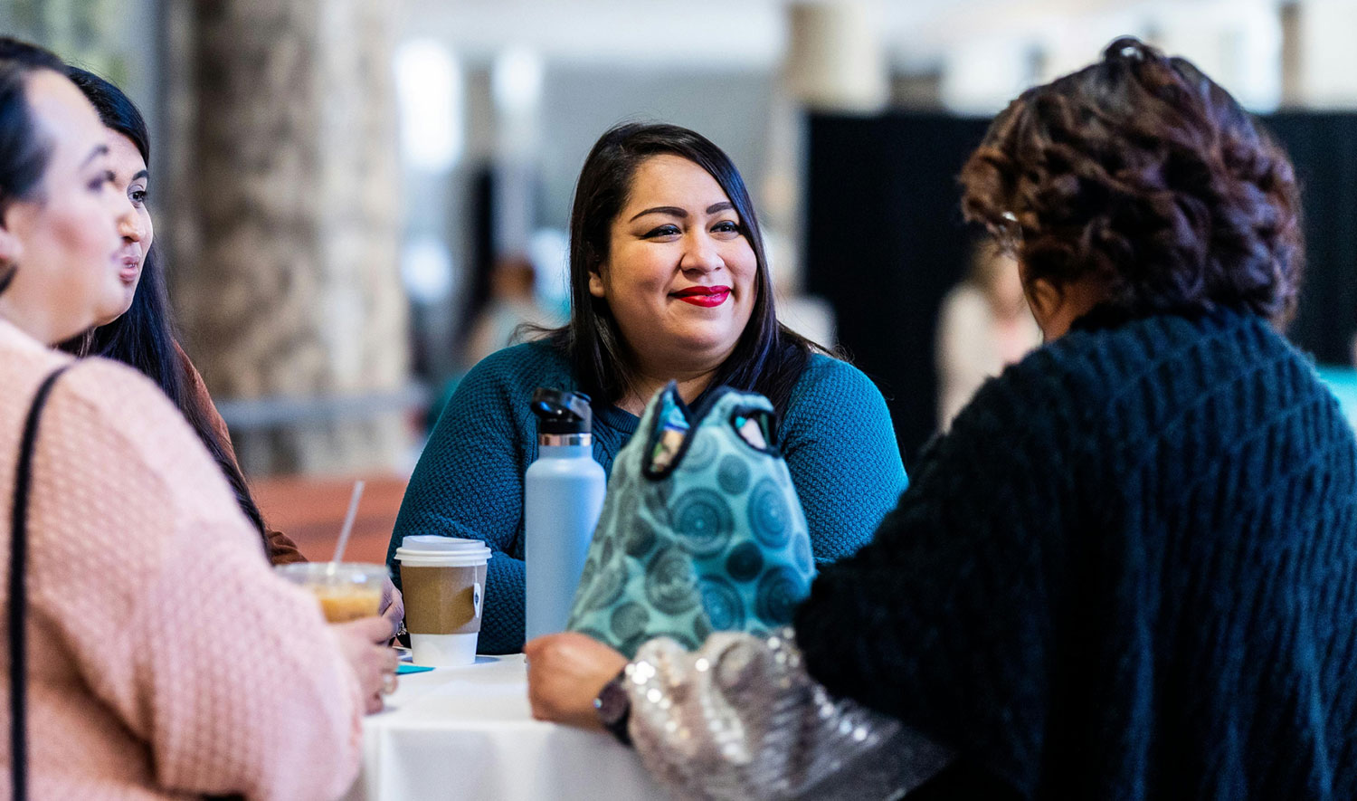 Small group of people engaging in conversation around a table with waters and coffees on it.