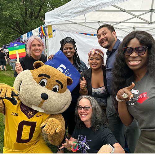 Staff and mascot smiling and pointing at camera