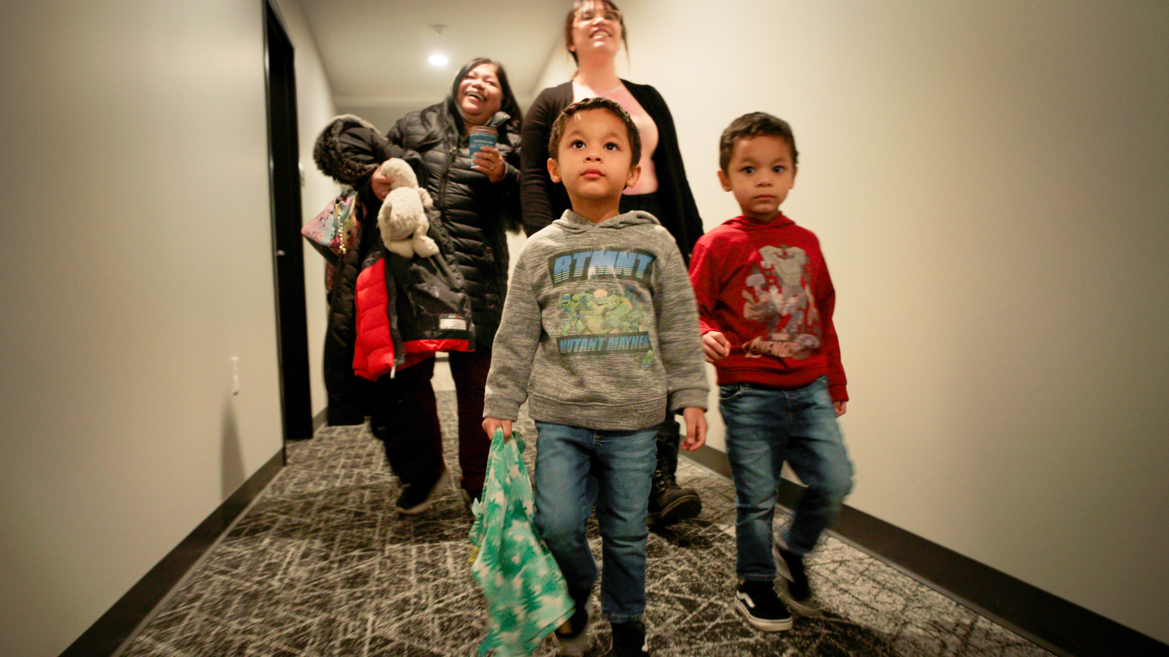 Two adults and two children carry their belongings through a hallway.