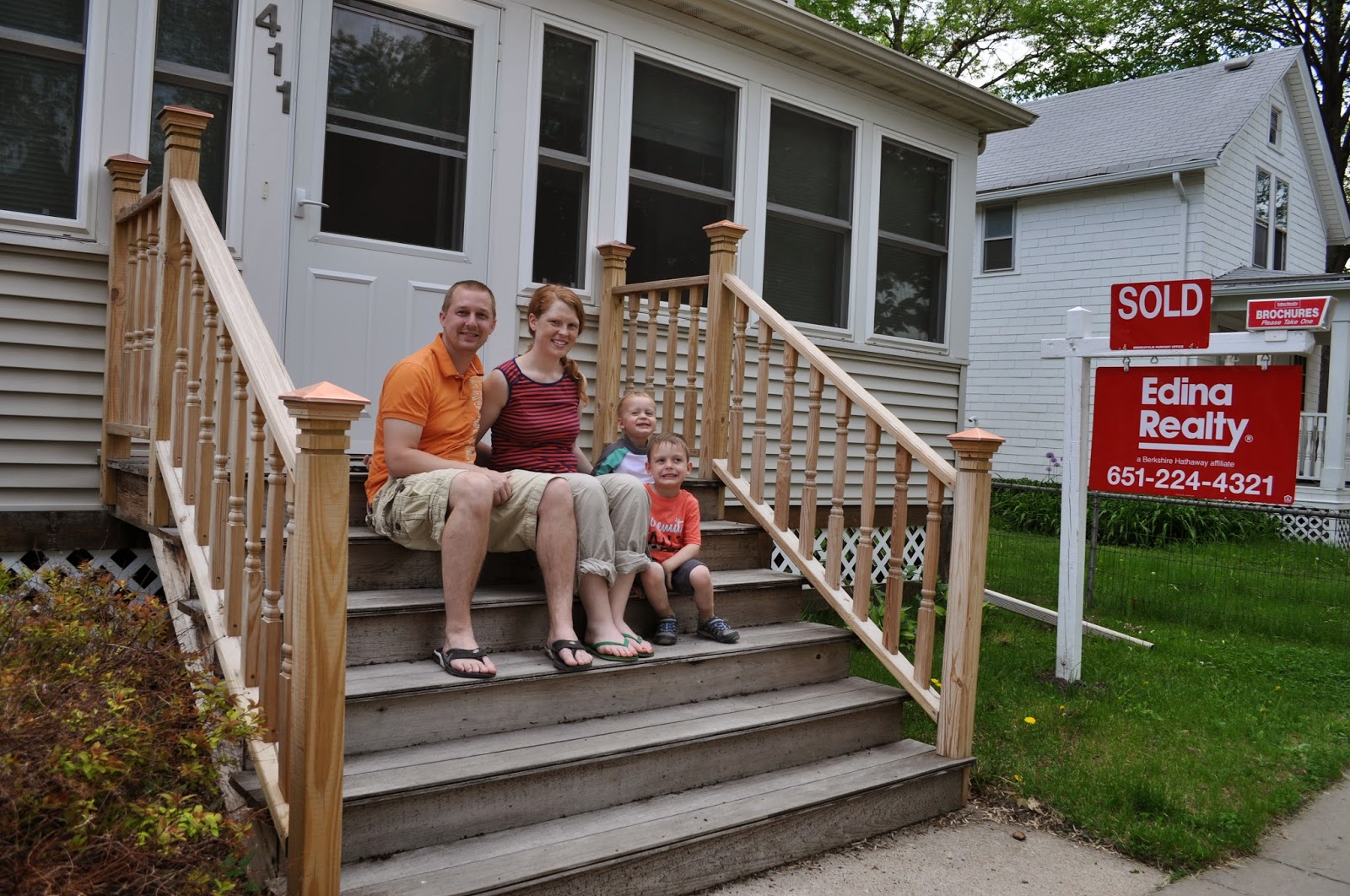 Couple and two kids on front steps with sold sign