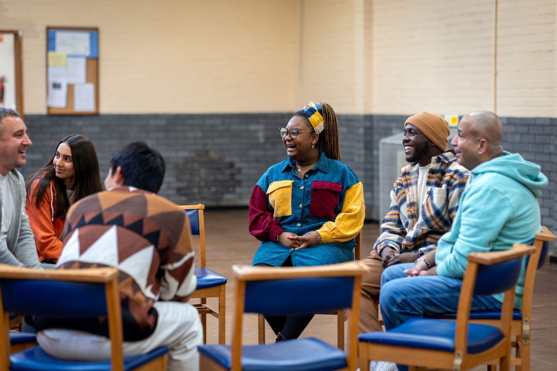 Diverse group of participants laughing and engaging while sitting in a circle of chairs in a large community setting.